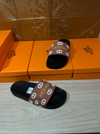 Black slide sandals with brown Hermes logo strap, one pair on boxes
