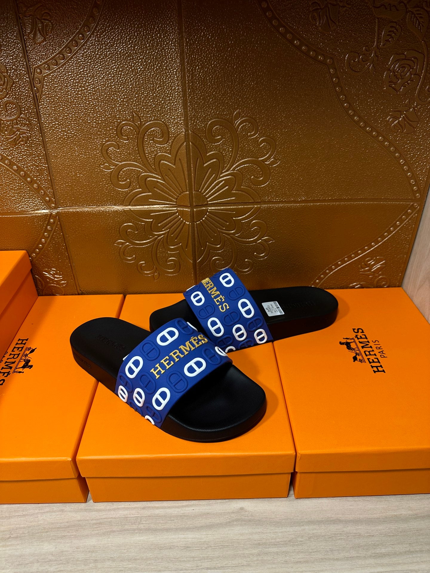 Black slide sandals with blue Hermes-pattern strap and open-toe silhouette.