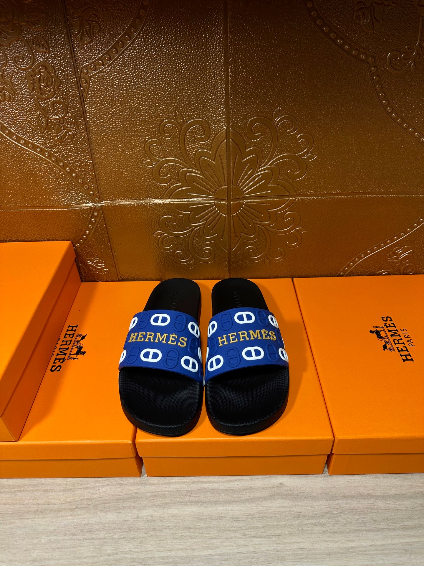 Black slide sandals with blue Hermes-pattern strap, flat footbed and wide band.