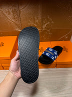 Black sandal outsole held in hand, textured pattern with repeated Hermes lettering.