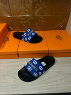 Black slide sandals with blue Hermes-pattern strap, pair laid with straps crossed.