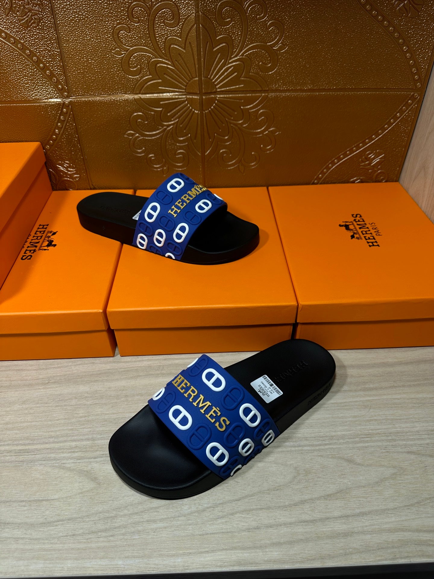 Black slide sandals with blue Hermes-pattern strap, pair laid with straps crossed.