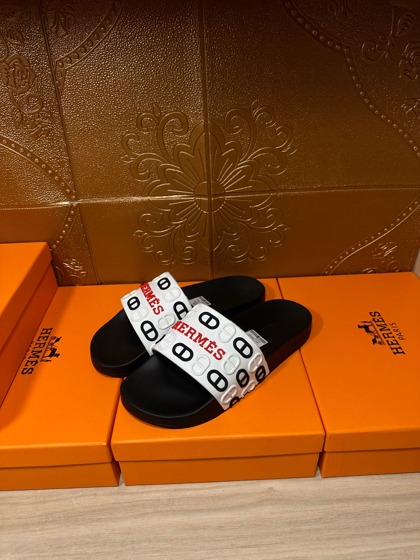 Black slide sandals with white patterned strap and Hermes logo.