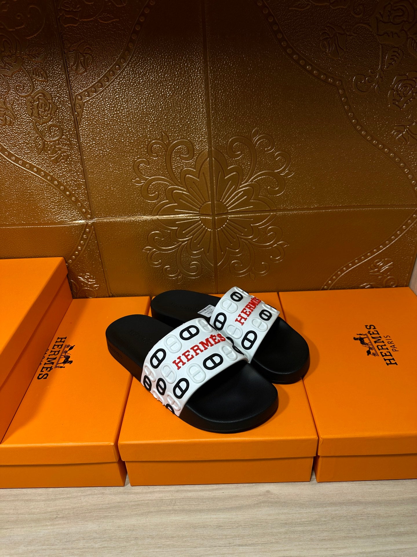 Black slide sandals with white strap featuring repeated Hermes marks.