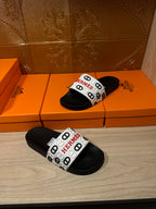 Black slide sandals with white Hermes logo strap, side view.