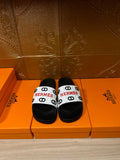 Black slide sandals with white logo strap and Hermes branding.