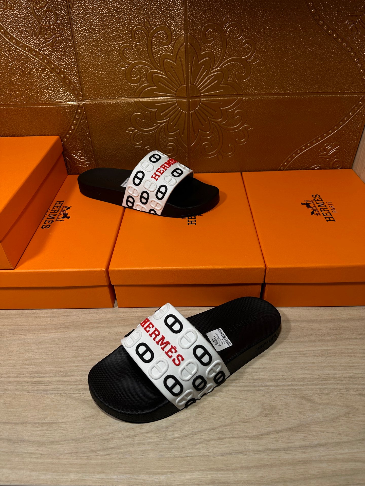 Black slide sandals with white Hermes logo strap, laid on display boxes.