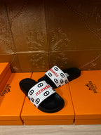 Black slide sandals with white Hermes logo strap on a single band.