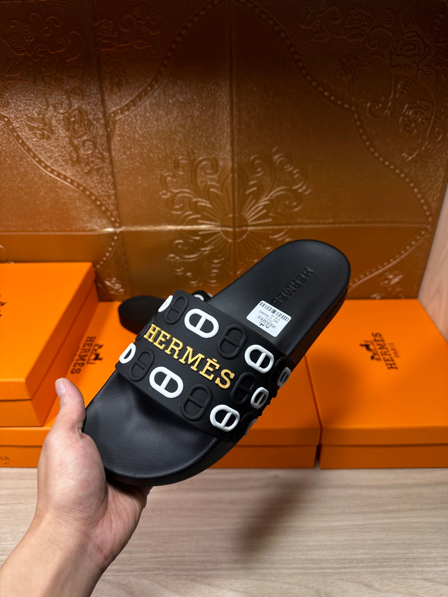 Black slide sandal with Hermes logo strap, front view held in hand