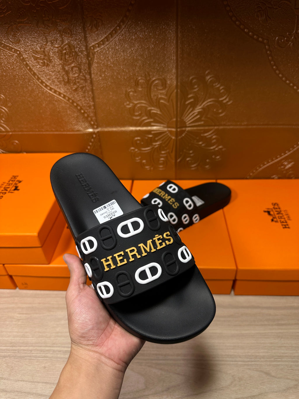 Black slide sandal with Hermes logo strap, held in hand