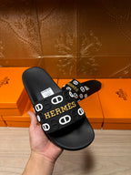 Black slide sandal with Hermes logo strap, held in hand