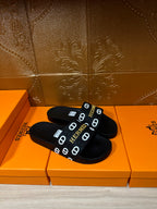 Black slide sandals with Hermes logo strap, angled pair view