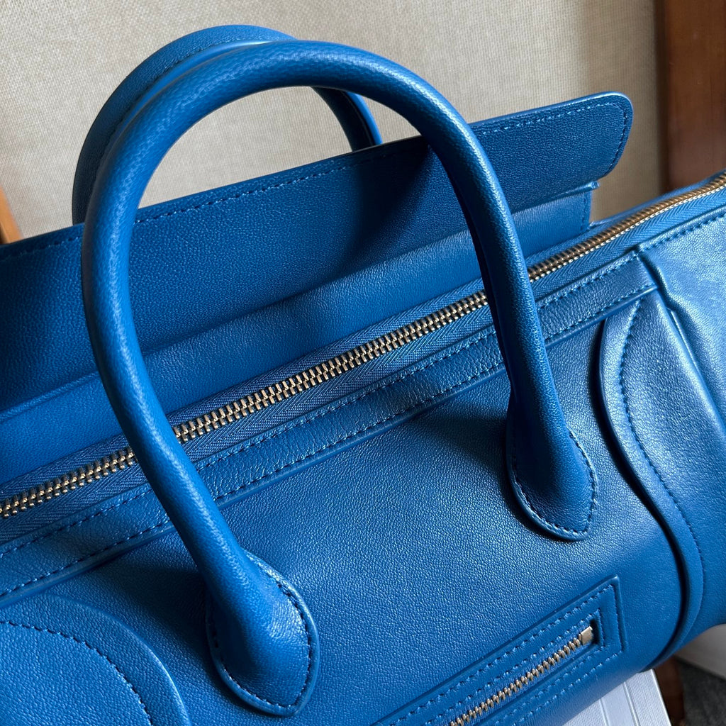 Blue leather top-handle bag with zipper pocket and curved handle stitching
