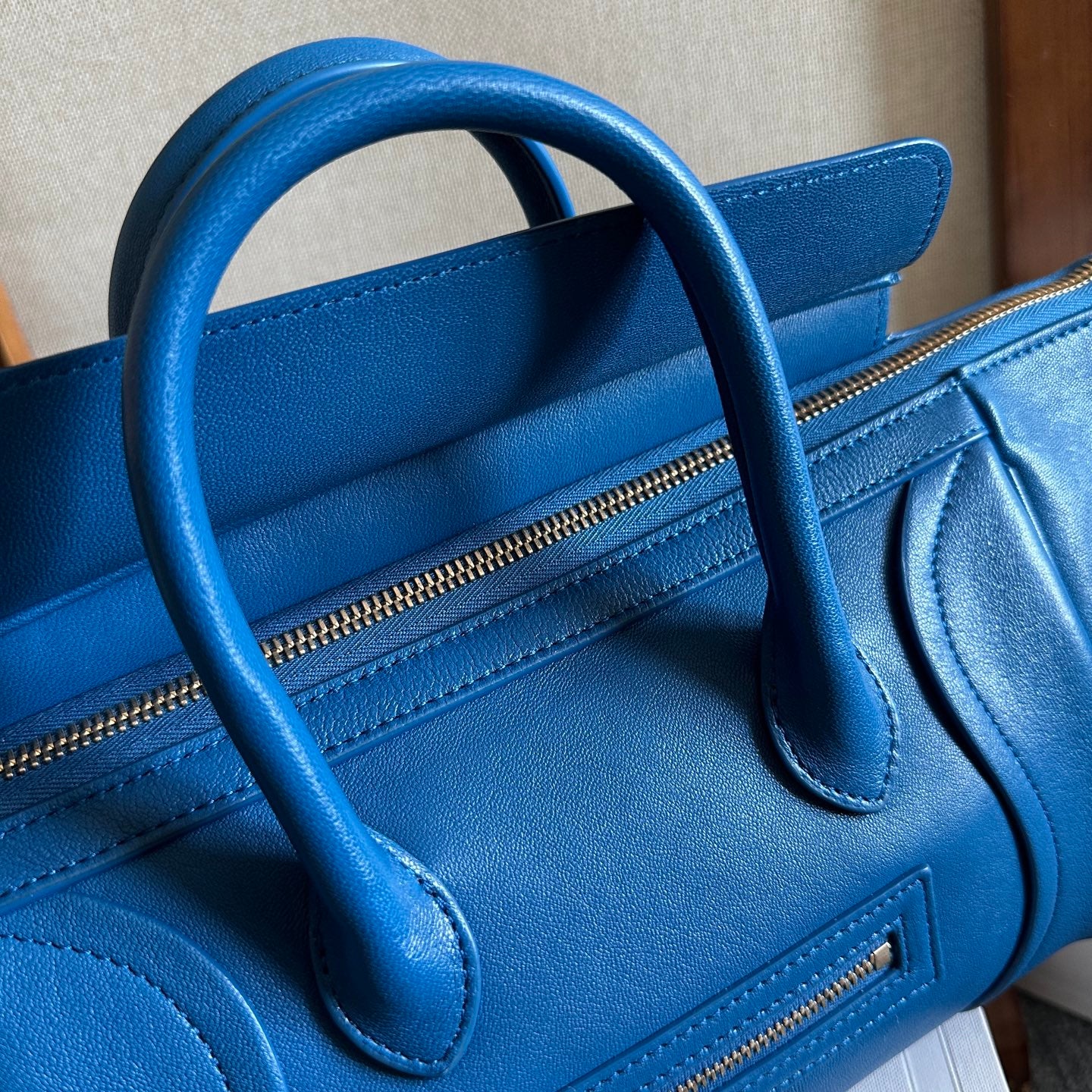 Blue leather top-handle bag with zipper pocket and curved handle stitching