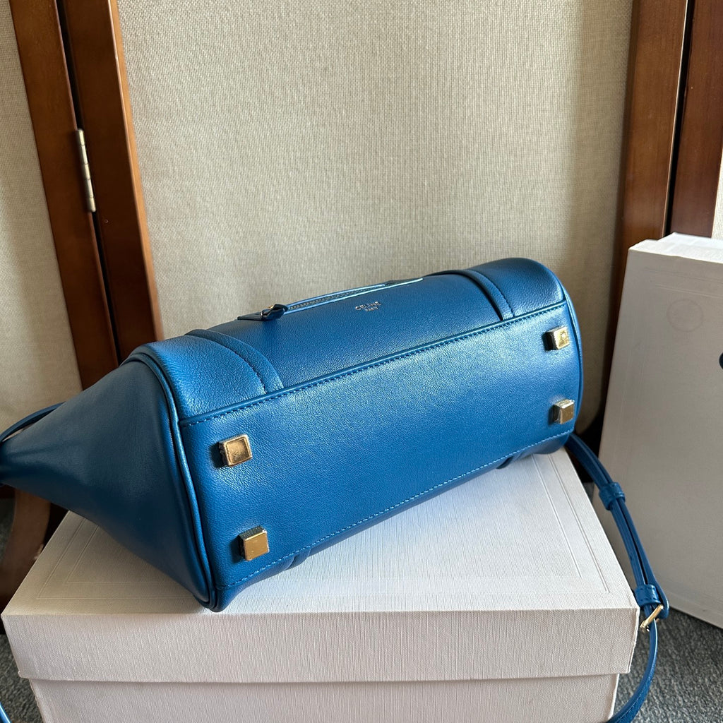Blue leather structured bag with top handle, side zipper, and gold feet