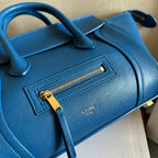 Blue leather bag front panel with embossed logo and gold zipper pull