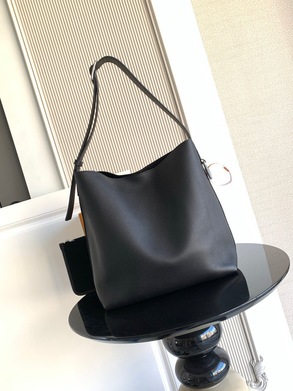 Black leather shoulder bag with curved top and long crossbody strap