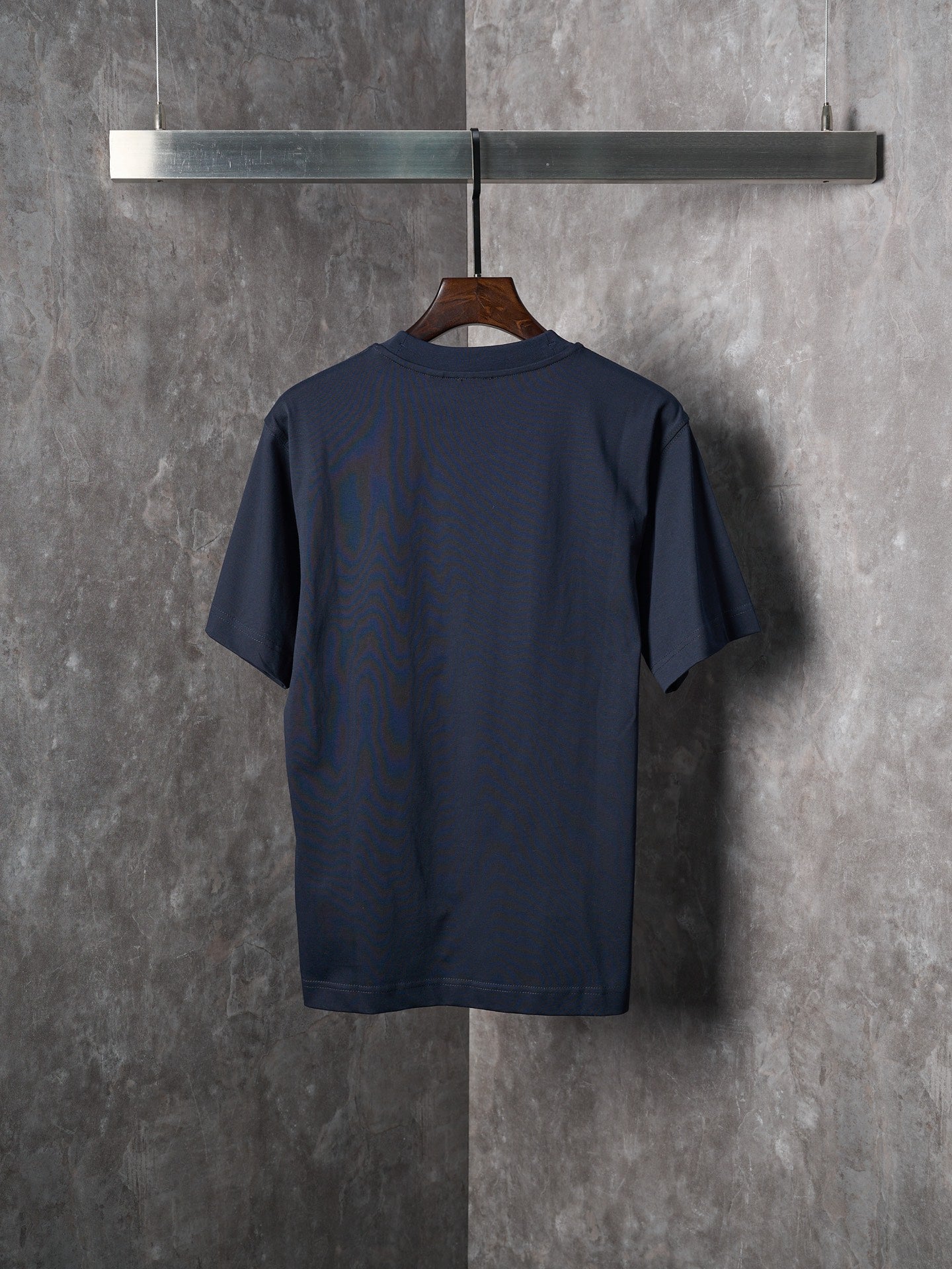 Navy crew-neck short-sleeve T-shirt shown from the back on a wooden hanger