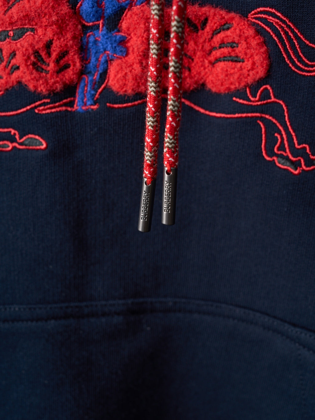 Navy hoodie drawstrings with metallic tips hanging from embroidered hood