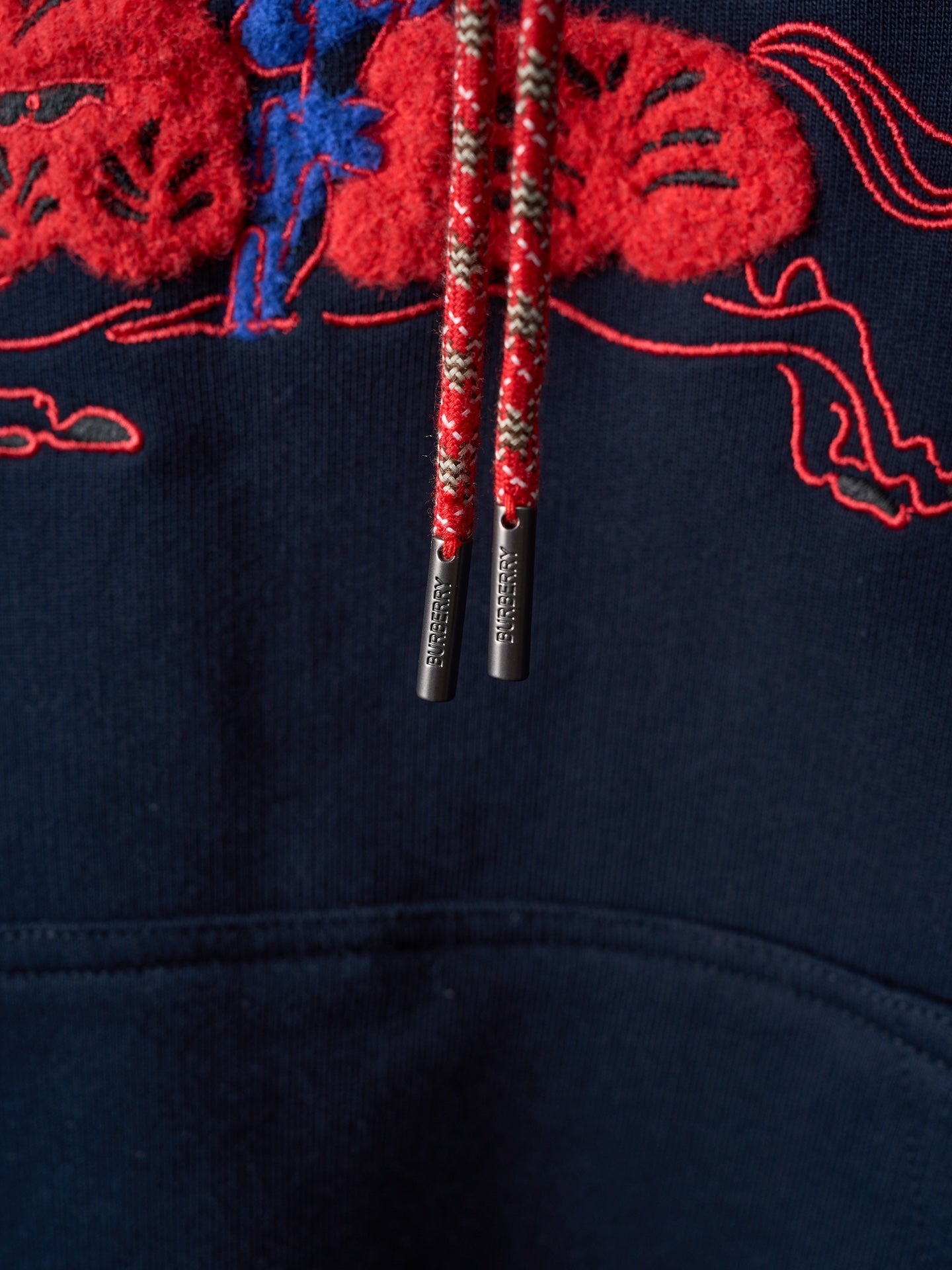Navy hoodie drawstrings with metallic tips hanging from embroidered hood