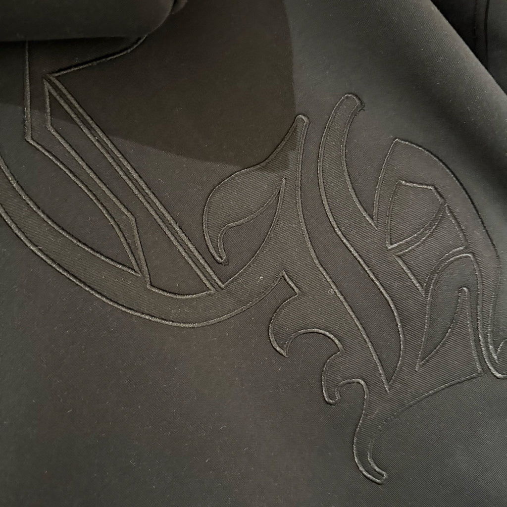 Dark hoodie front close-up with raised embroidered graphic across chest