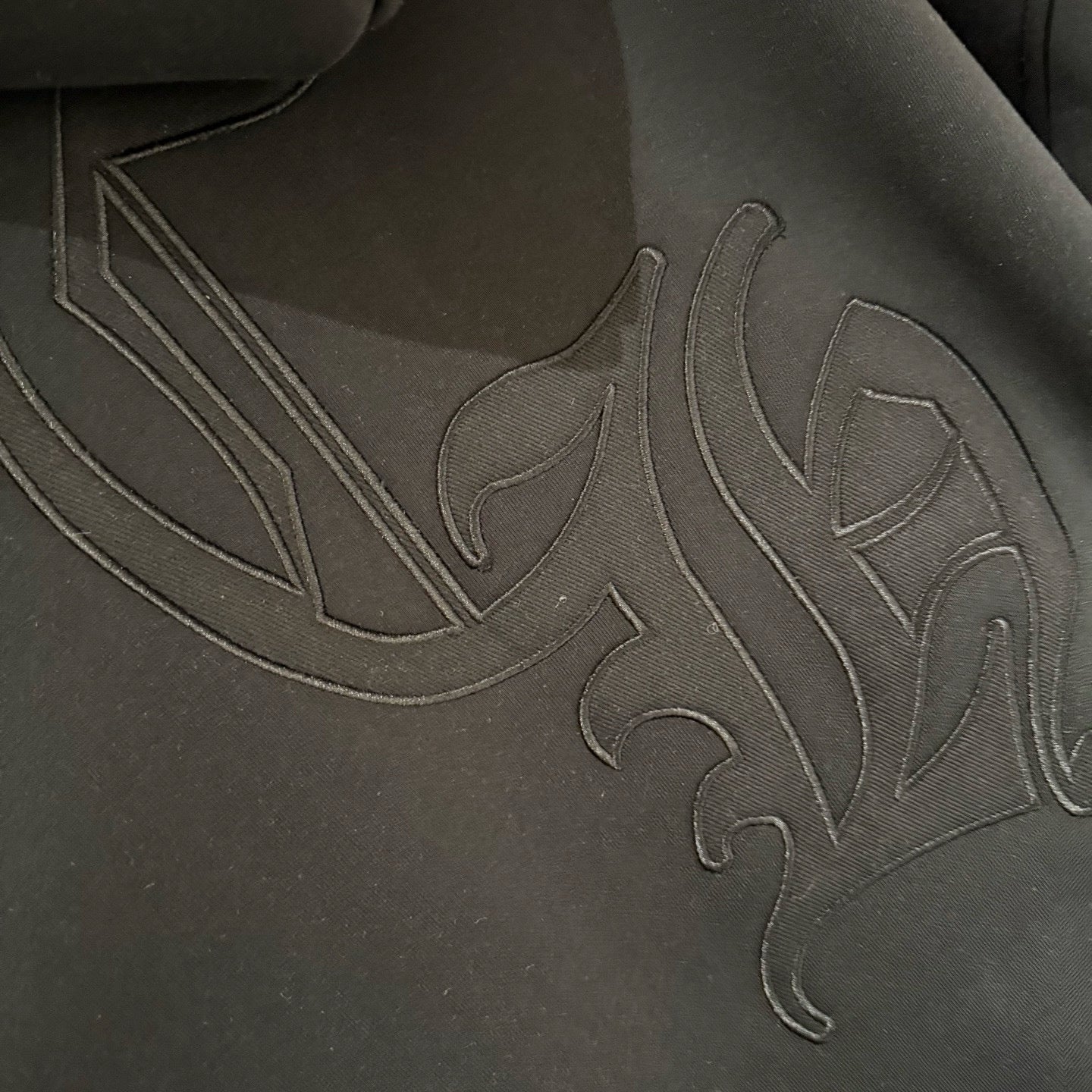 Dark hoodie front close-up with raised embroidered graphic across chest