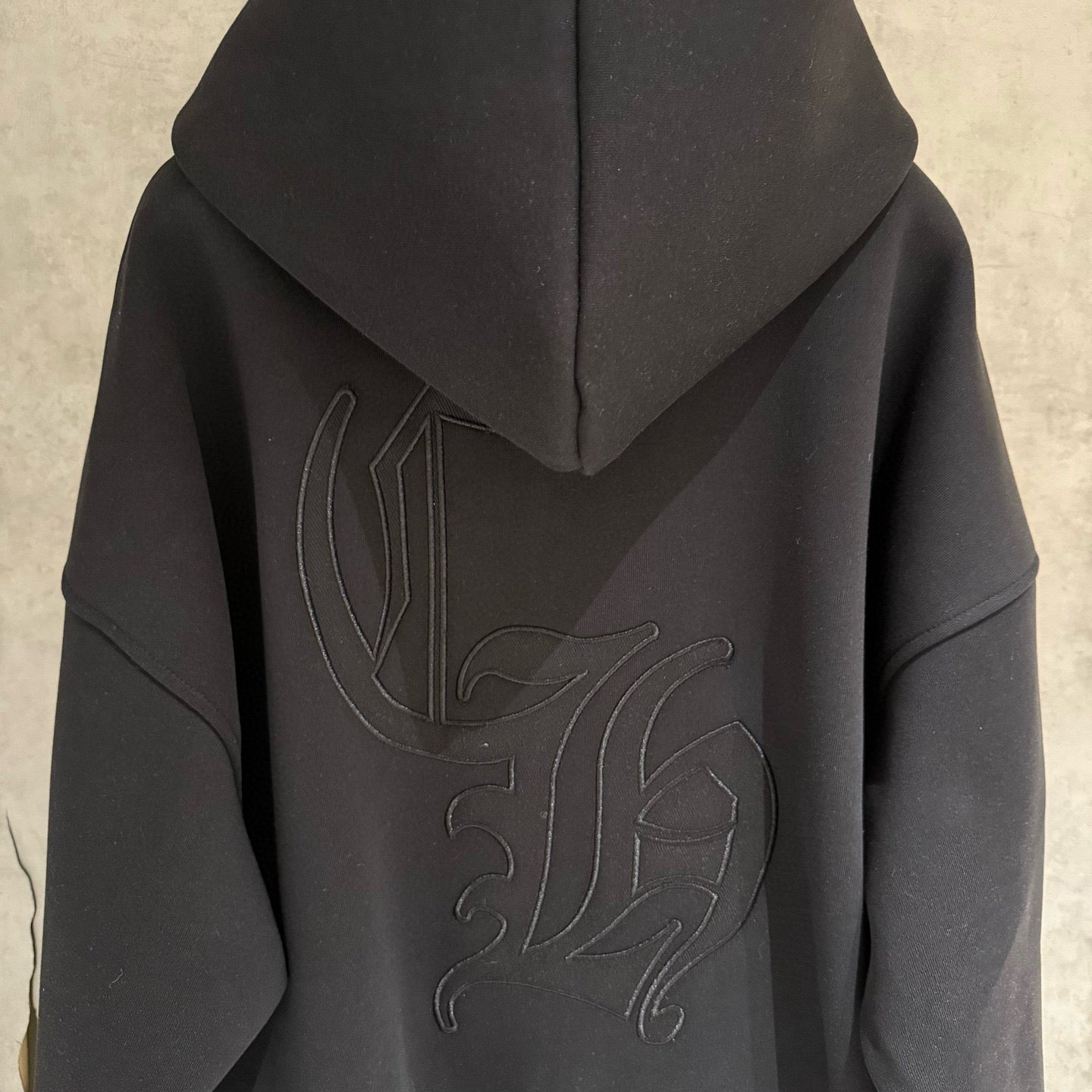 Dark hoodie back close-up with hood and raised embroidered graphic