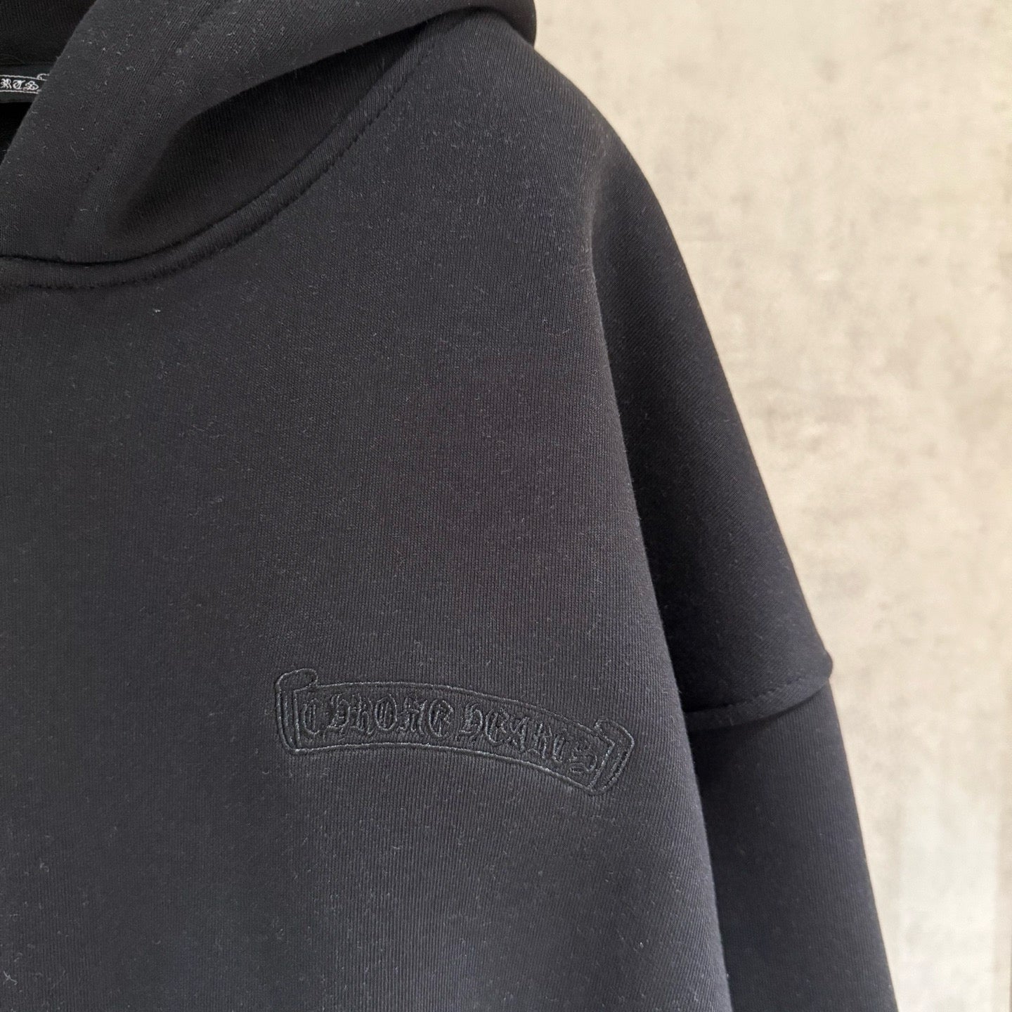 Dark hoodie sleeve close-up with small embossed logo detail