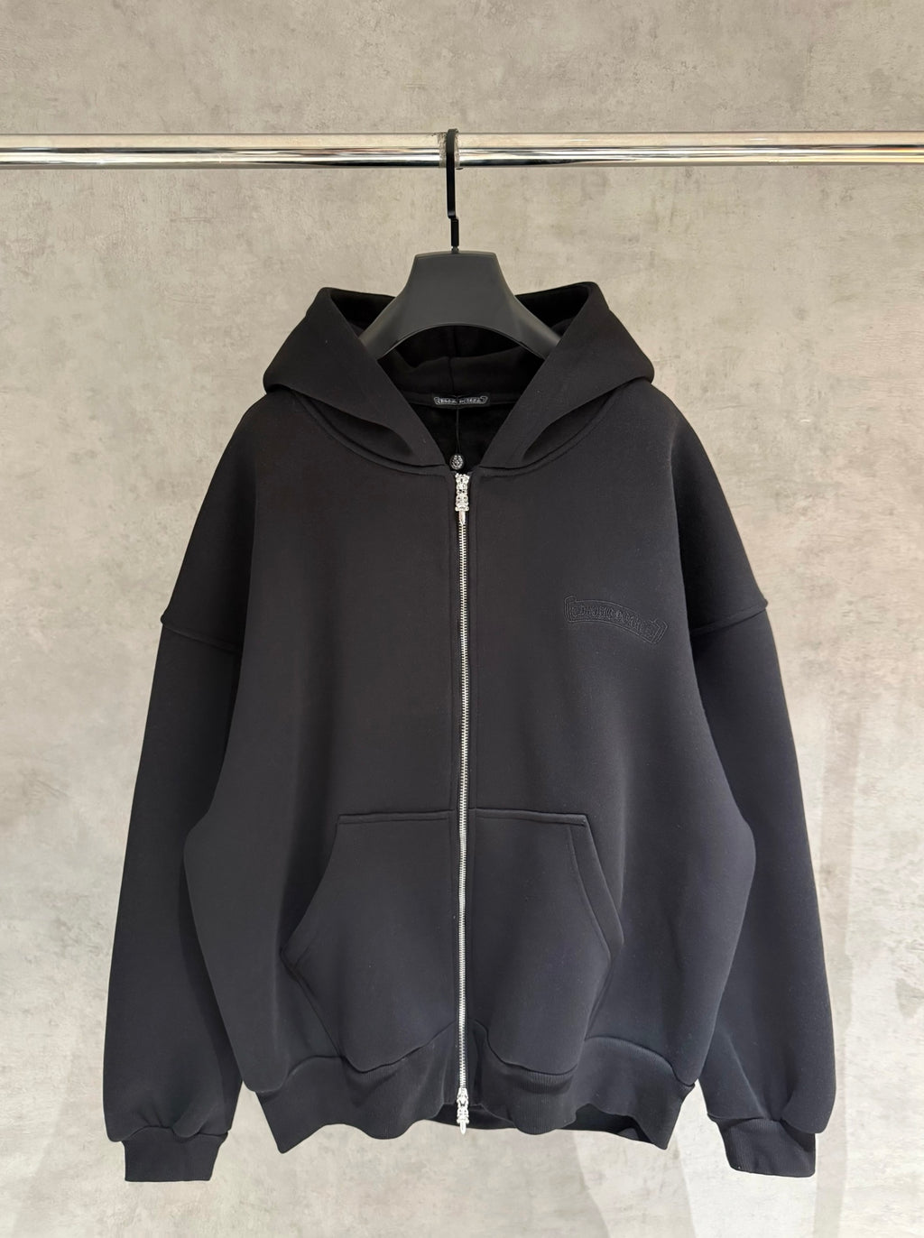 Dark zip-up hoodie with hood and front kangaroo pocket, hanging on a hanger