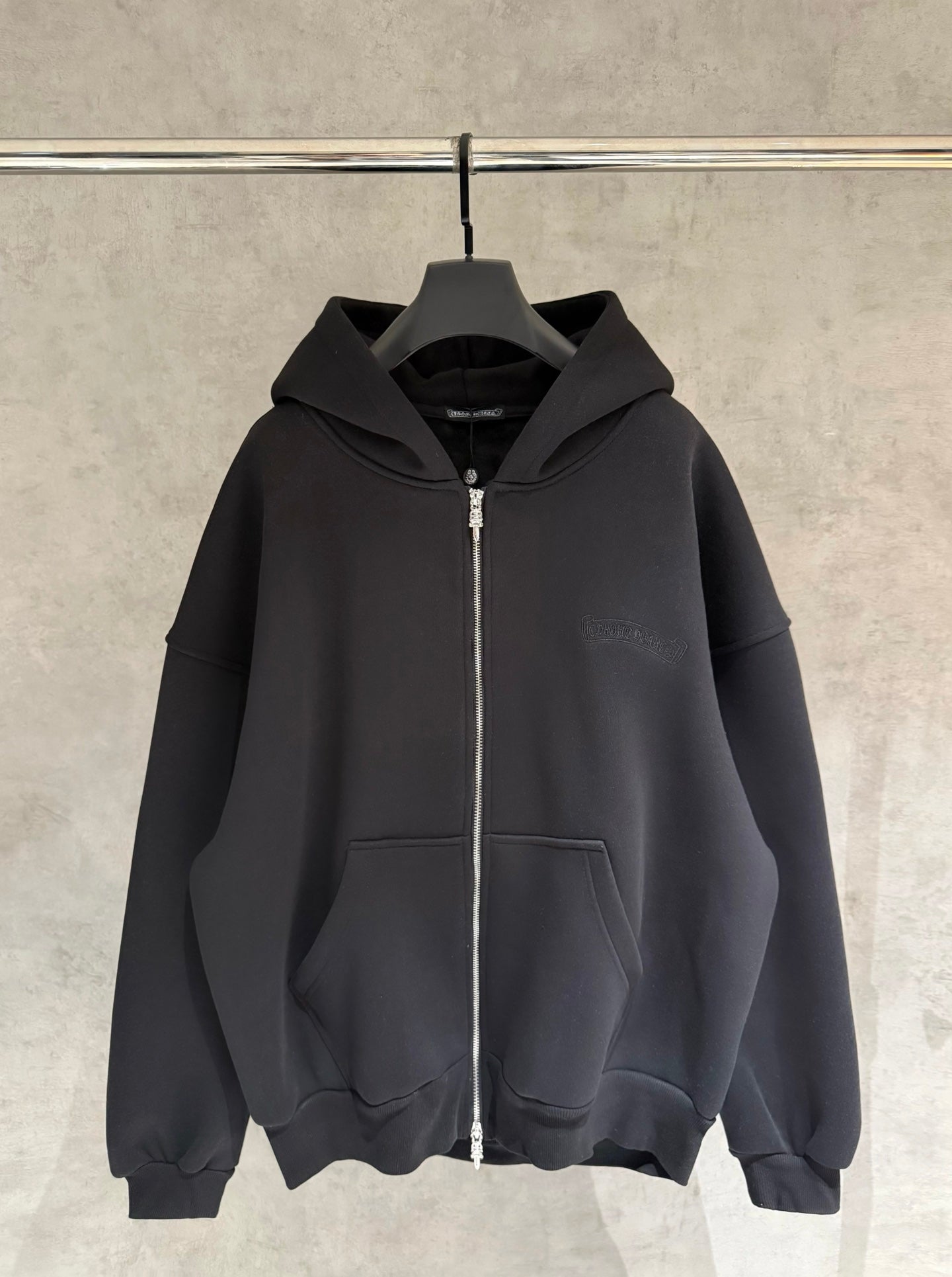 Dark zip-up hoodie with hood and front kangaroo pocket, hanging on a hanger
