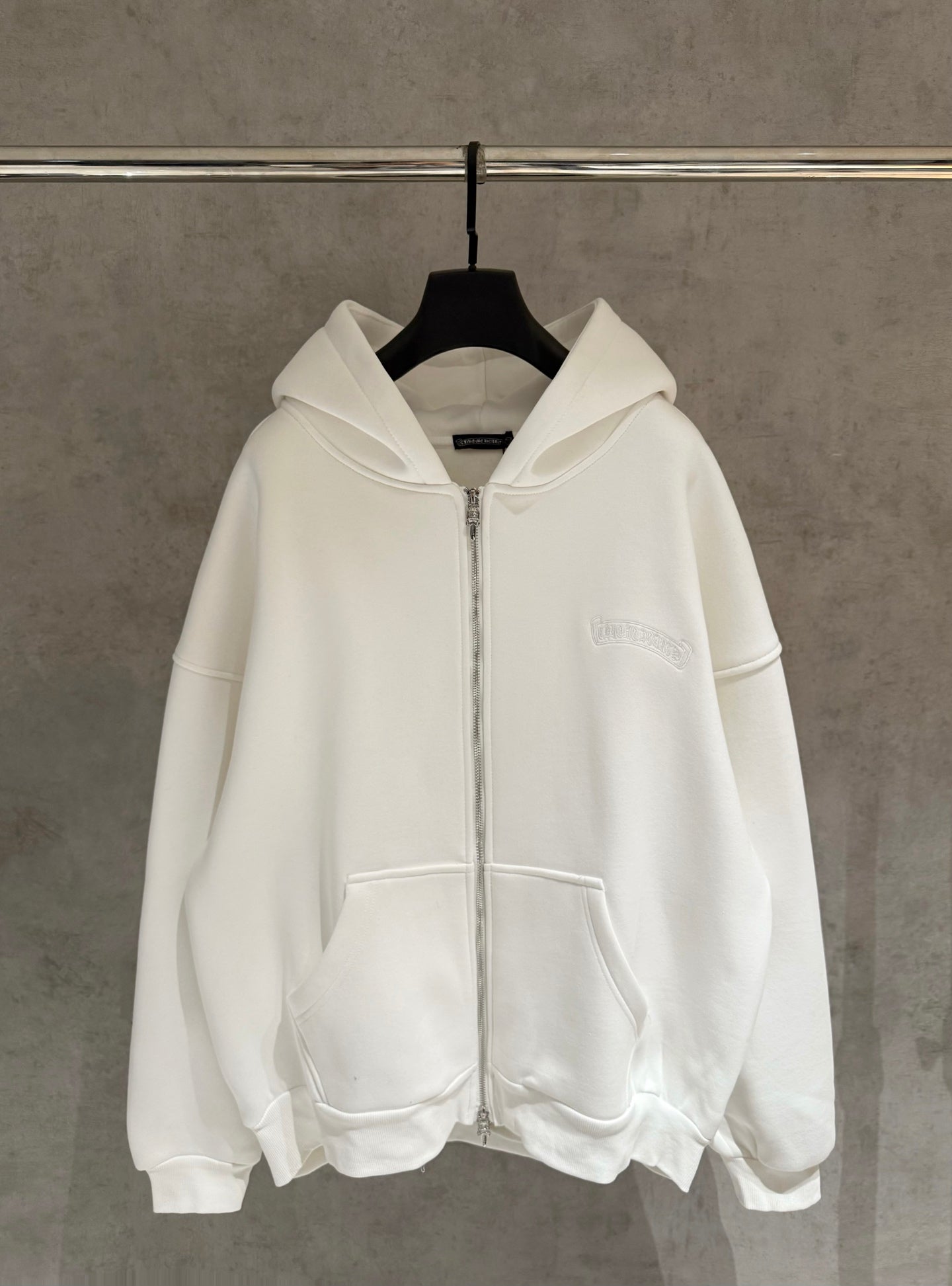 White zip-up hoodie with hood and front pockets on hanger