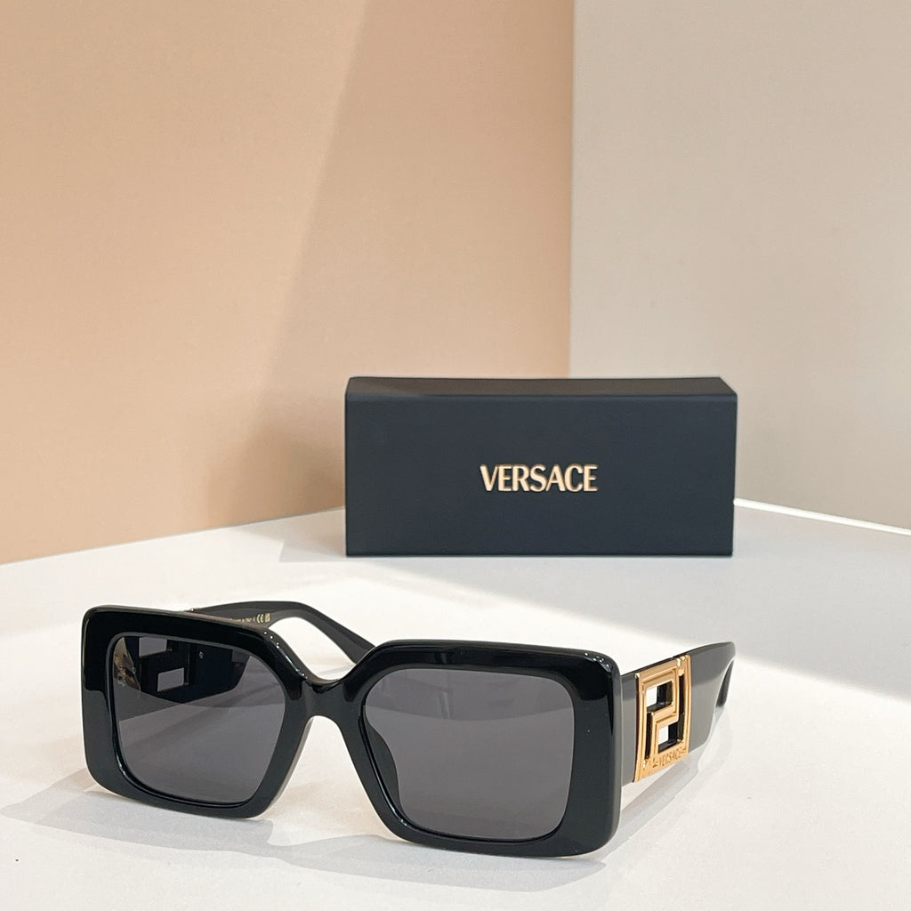 Black square sunglasses with gold Versace logo temples and gray lenses.