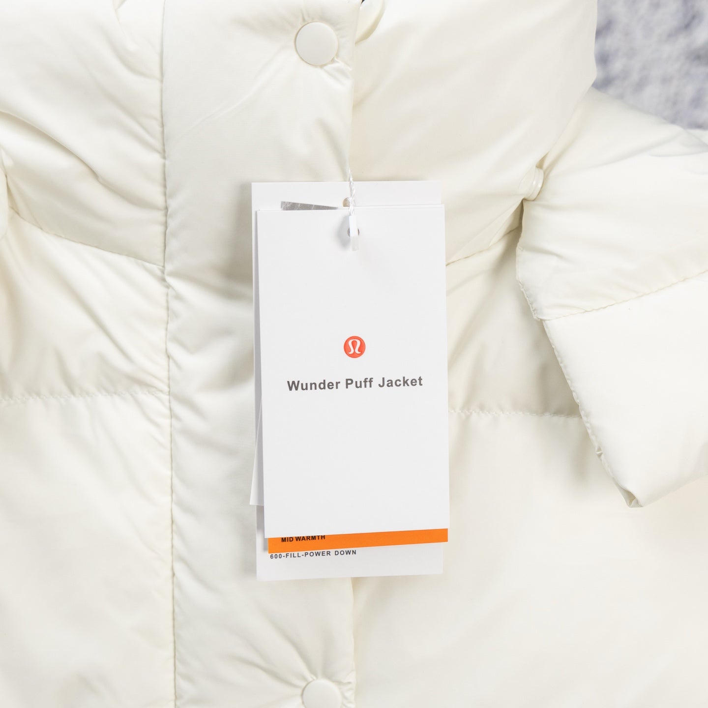 White puffer jacket close-up with snap button front and hanging product tag