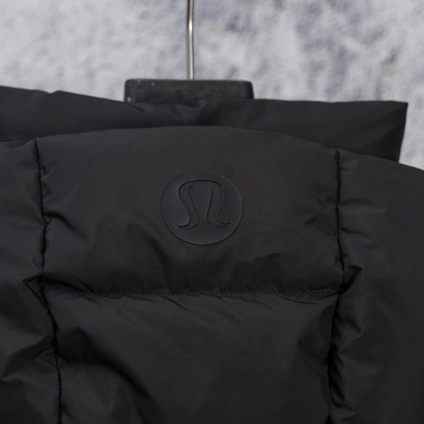 Black puffer vest back with embossed logo badge near collar