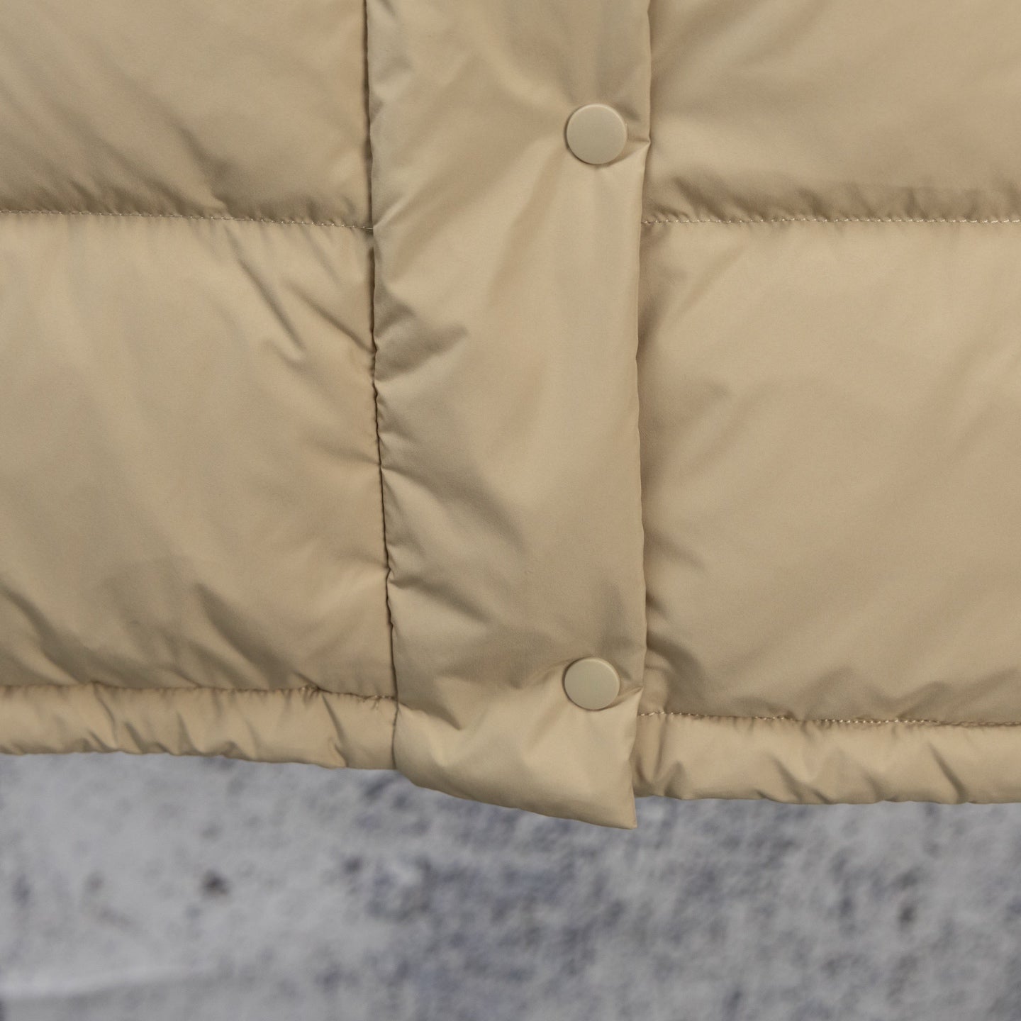 Beige puffer jacket front with two snap buttons and quilted lower panel