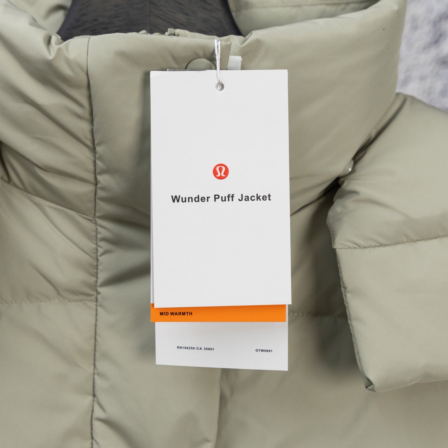 Light sage puffer vest fabric close-up with hanging “Wunder Puff Jacket” tag