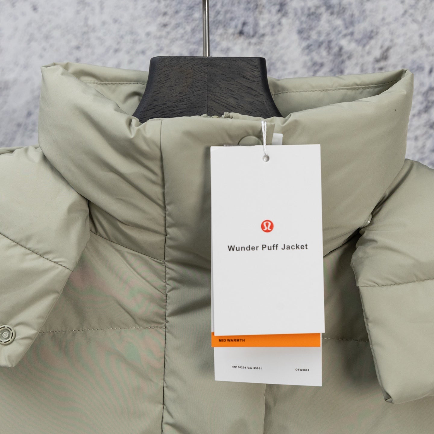 Light sage puffer vest with standing collar and hanging brand tag at the chest