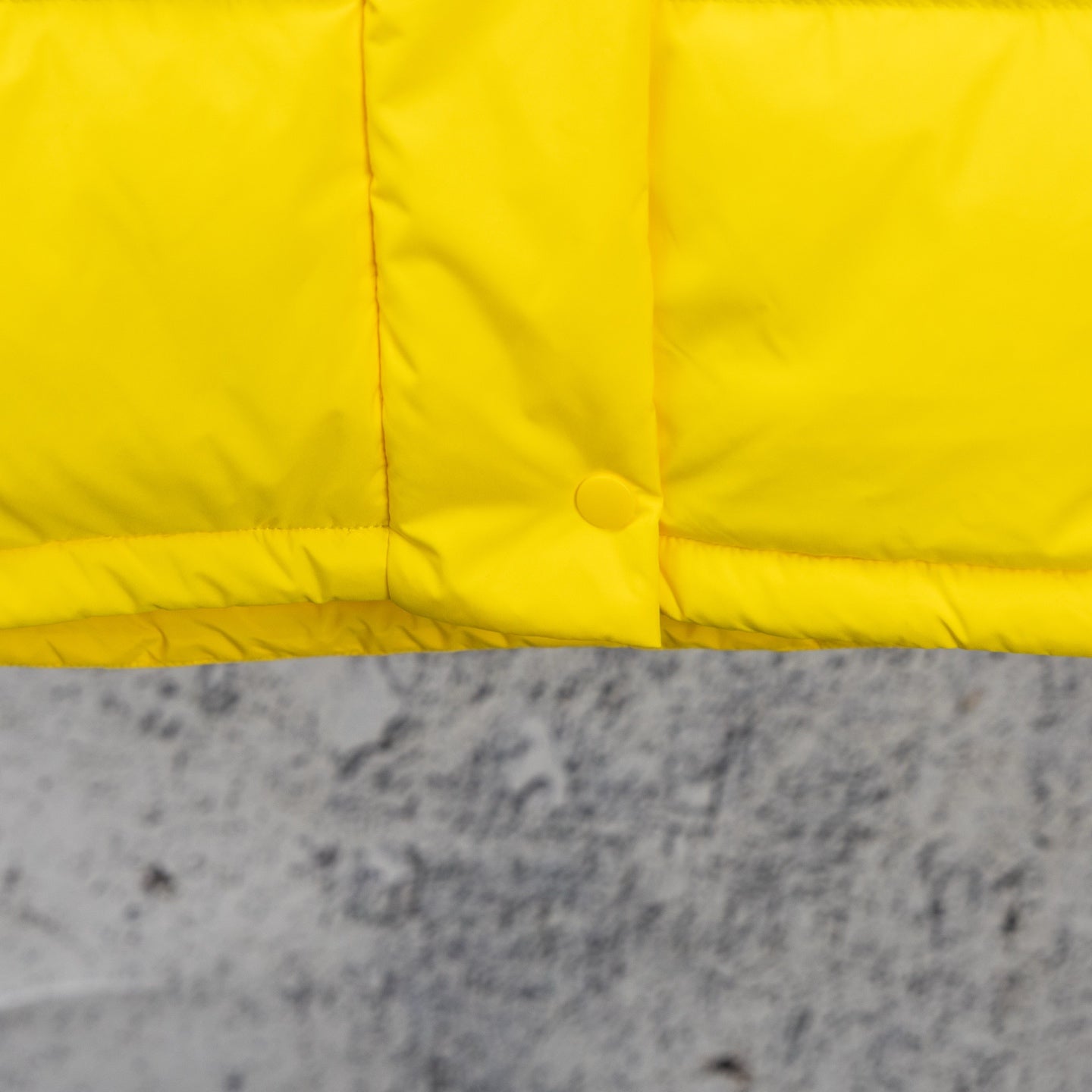 Yellow puffer jacket lower front panel with snap and stitched seams