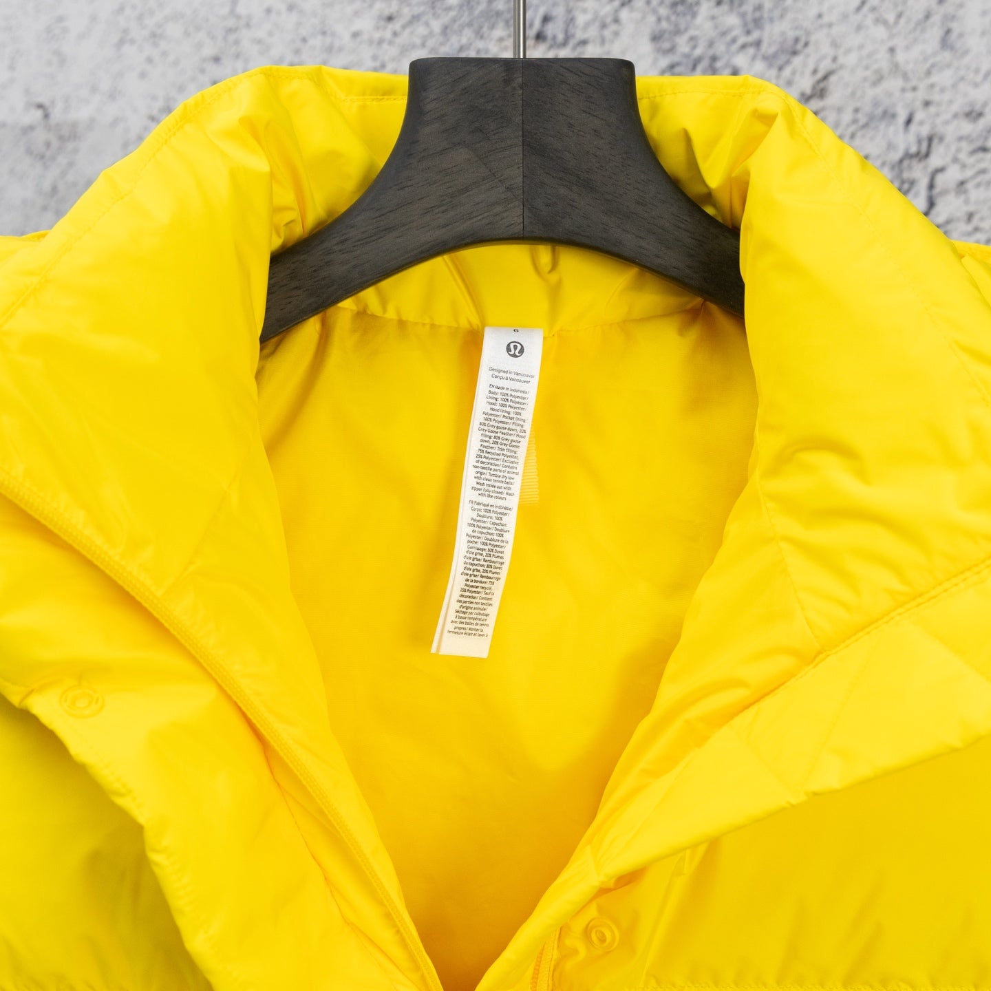 Yellow puffer jacket with open hood and interior label on hanger