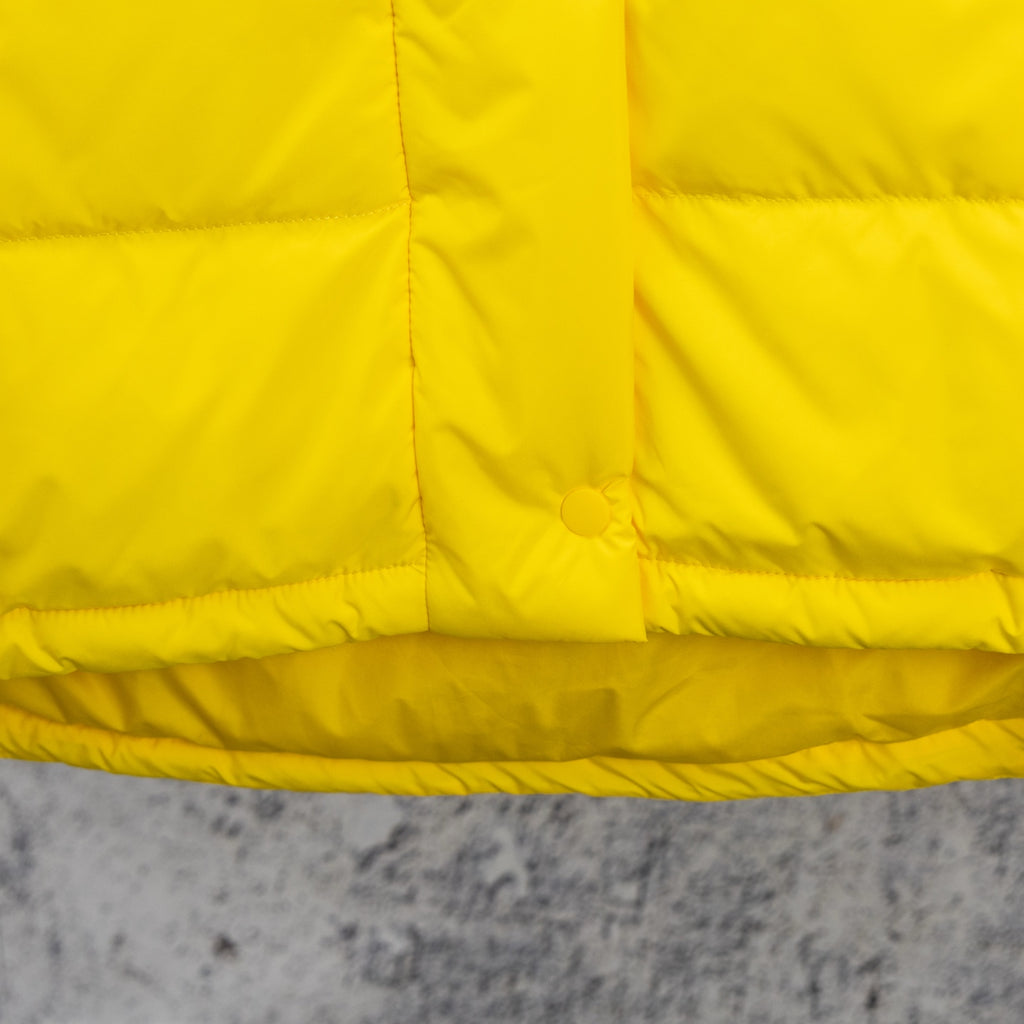 Yellow puffer jacket front yoke with horizontal quilting and circular snap