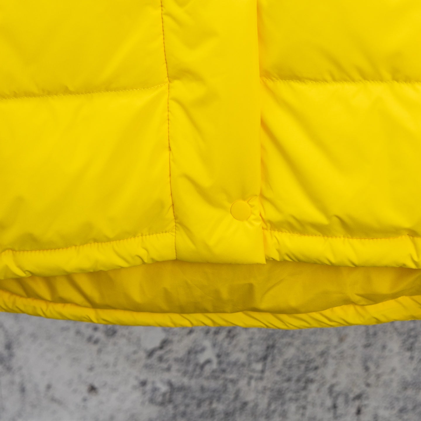 Yellow puffer jacket front yoke with horizontal quilting and circular snap