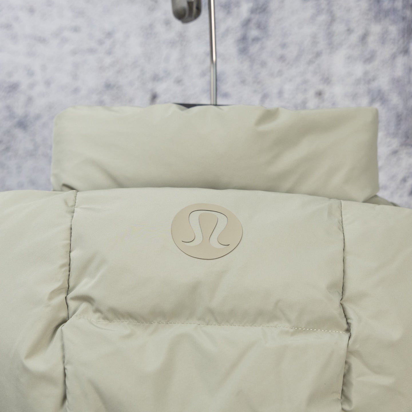 Beige hooded puffer jacket with circular logo patch on upper back