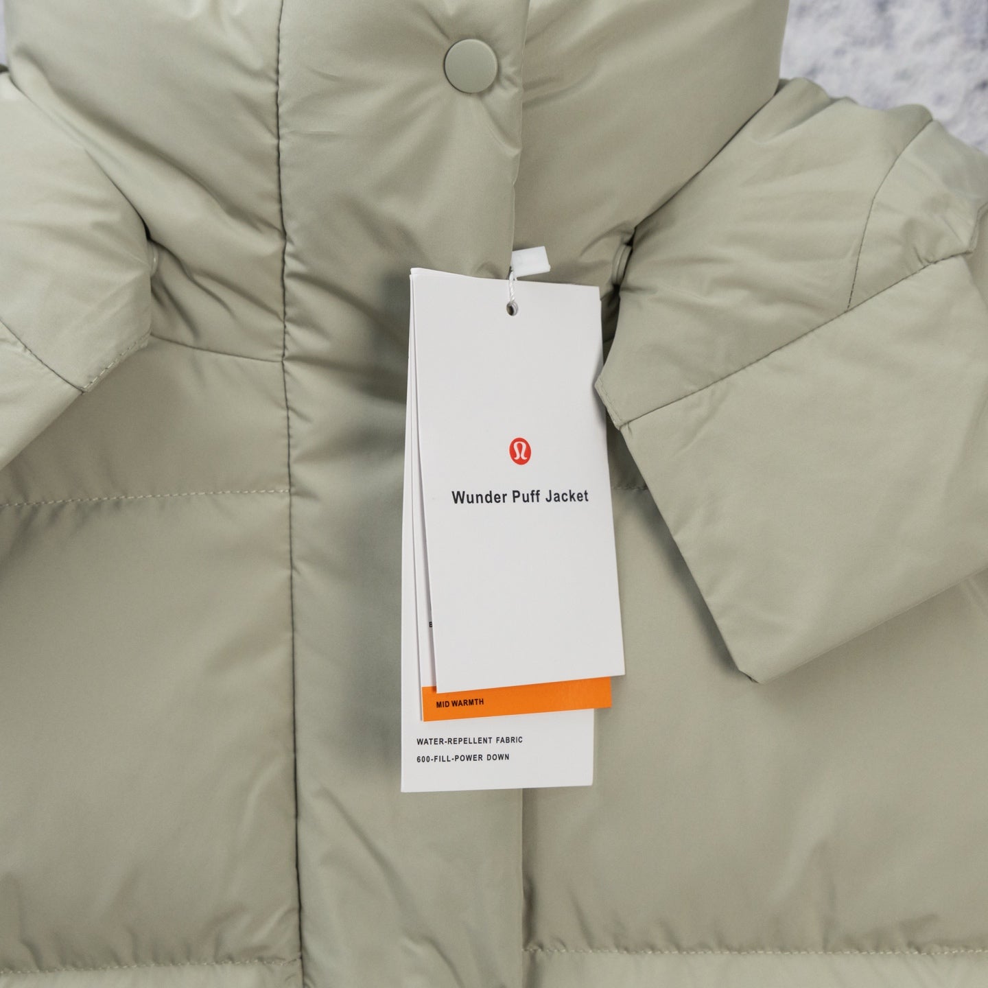 Light olive hooded puffer jacket with button placket and hanging product tag