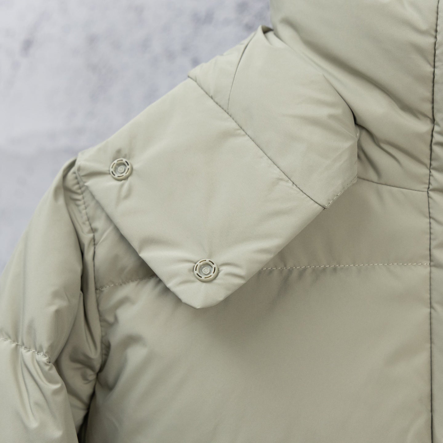 Light olive puffer jacket sleeve with metal snap button and stitched panel seams