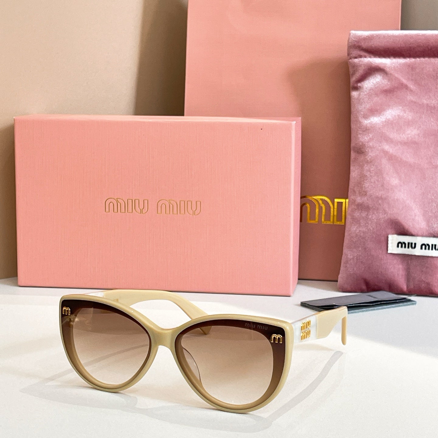 MiuMiu cat-eye sunglasses with cream frames and brown lenses.