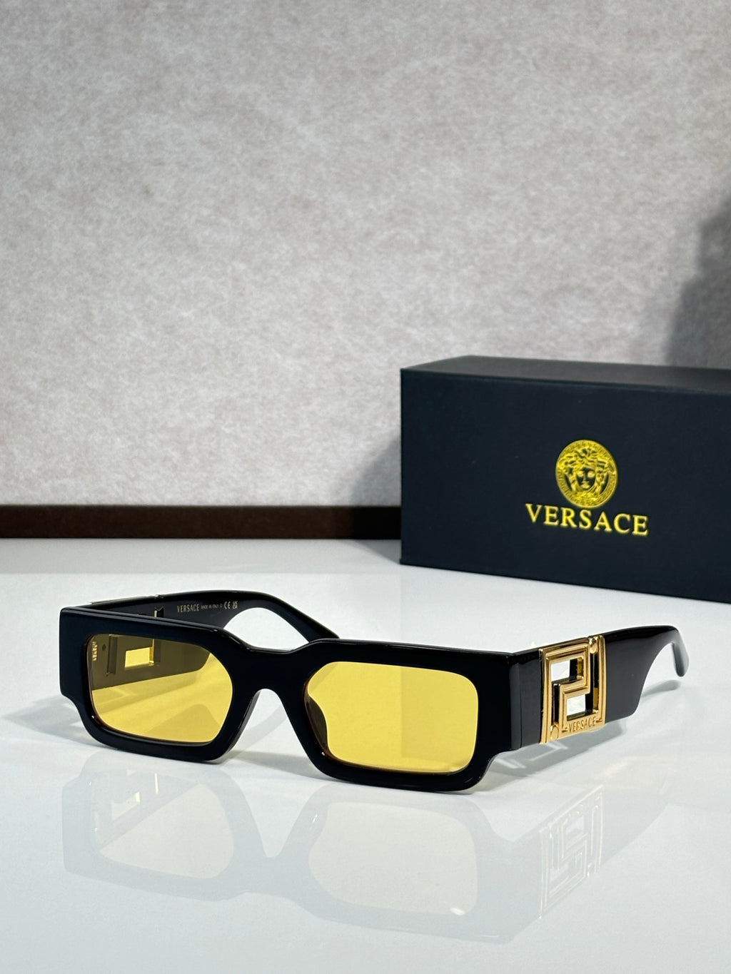 Rectangular sunglasses with black frames, yellow reflective lenses, gold logo temple detail