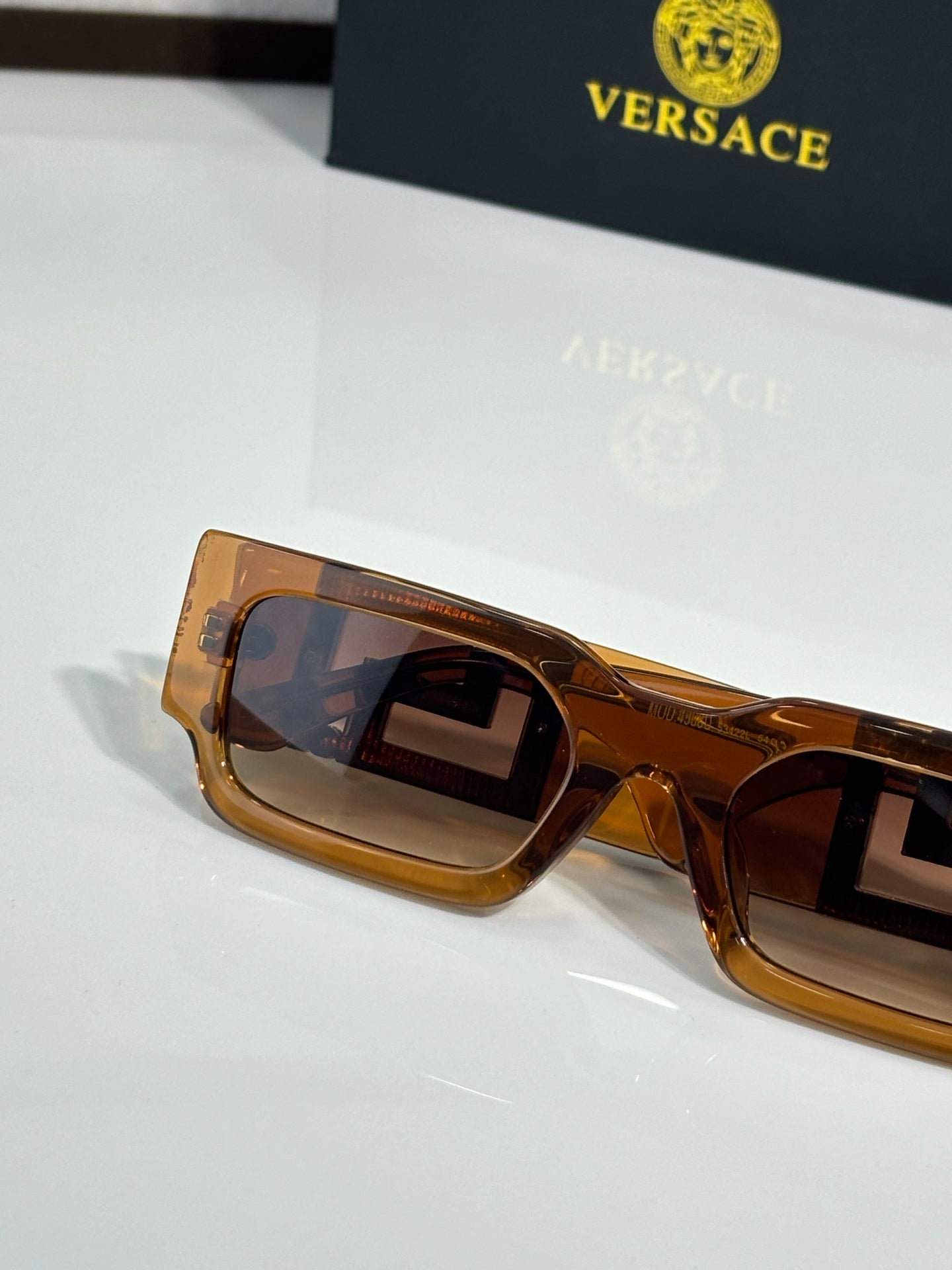 Rectangular sunglasses side view with amber frames and tinted lenses, gold logo detail