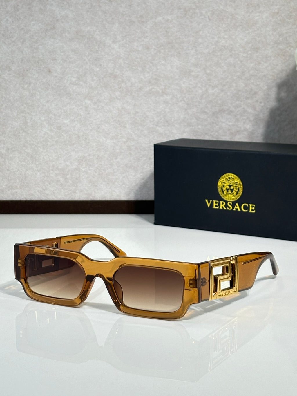 Rectangular sunglasses with amber brown frames, brown tinted lenses, gold logo temples