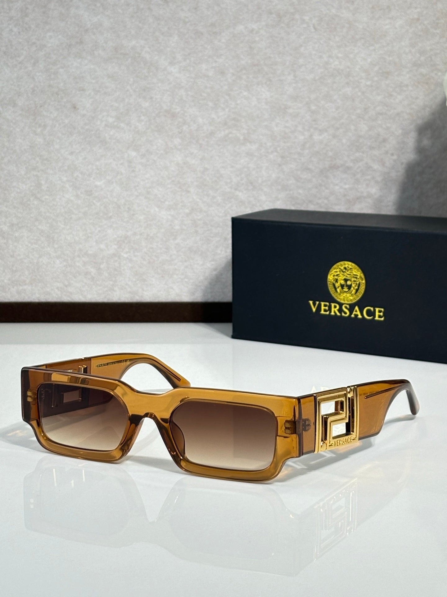 Rectangular sunglasses with amber brown frames, brown tinted lenses, gold logo temples