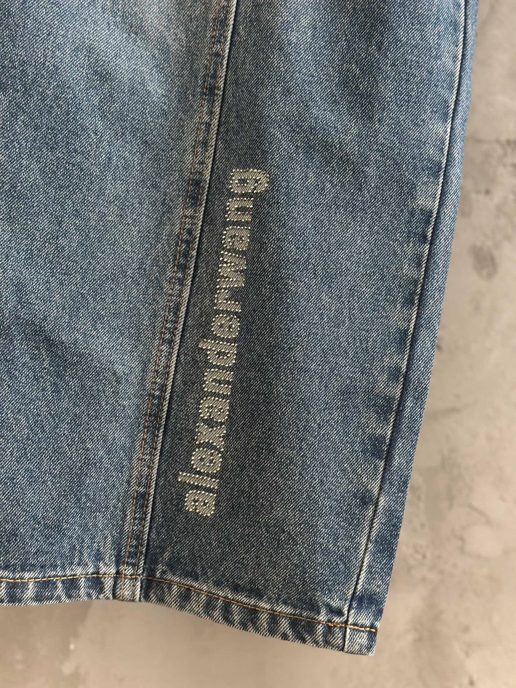 Blue denim pants with vertical “alexanderwang” label near hem